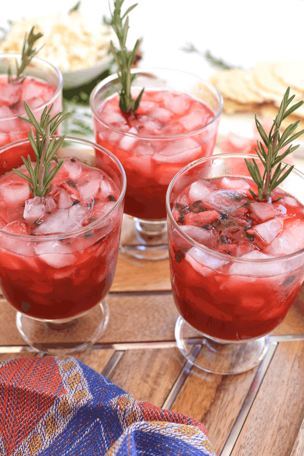 Close up of glasses holding red Blackberry Whiskey Lemoande Cocktails garnished with fresh rosemary.