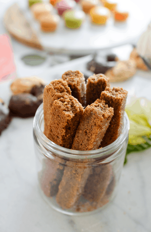 Close up of cookie sticks served in a small round glass jar on a party table. 