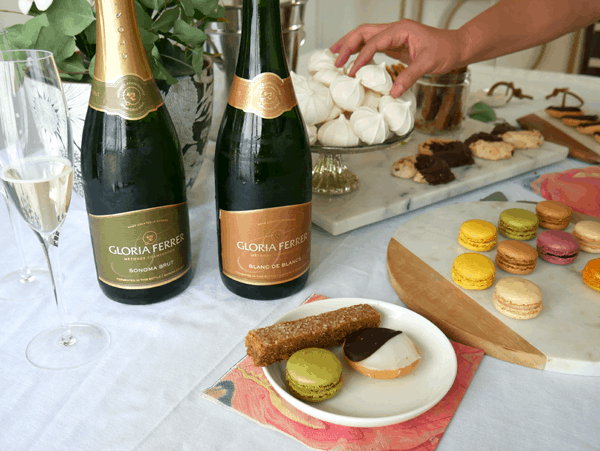 2 bottles of champagne on a table for a holiday cookie exchange with a small dessert plate filled with cookies.