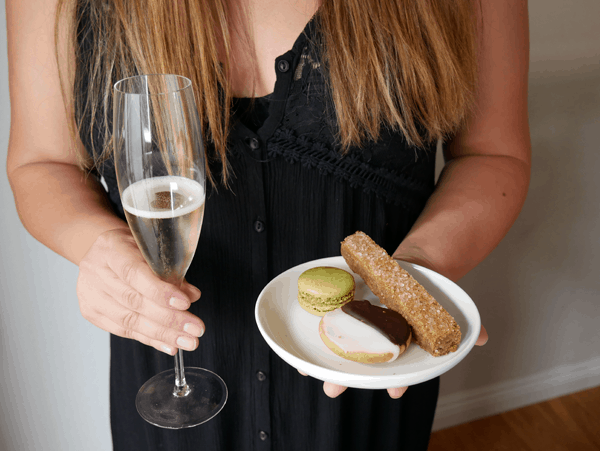 A woman holding a glass of champagne in one hand and small dessert plate with cookies in the other hand.