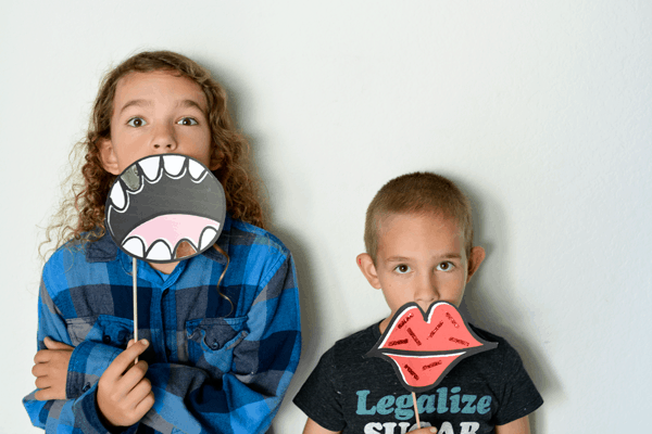 Two kids holding up funny mouth photo booth props in front of their faces. 