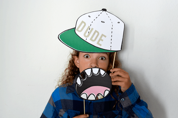 Kid holding a mouth and hat photo booth prop in front of his face. 