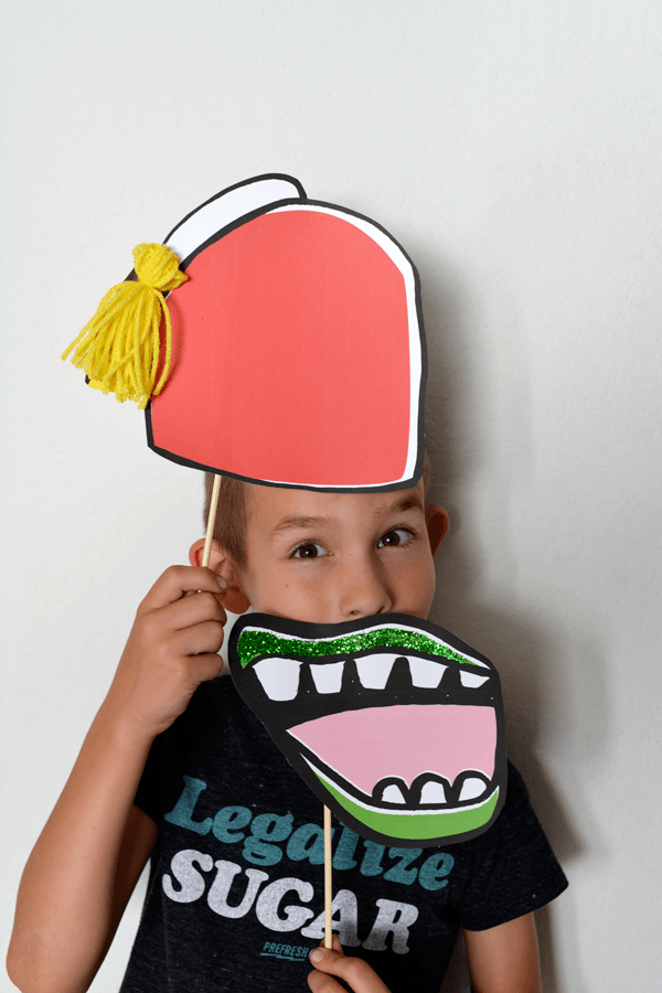 Kid holding a mouth and hat photo booth prop up to his face. 