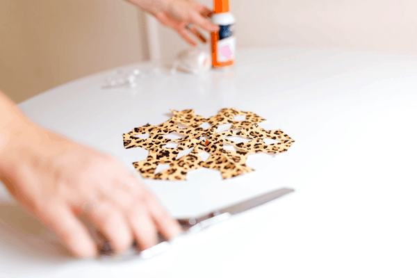 A leopard print snowflake on a table and a woman grabbing a pair of scissors.