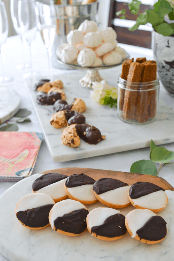 A plate of black and white cookies on a table next to other trays of cookies for a party.