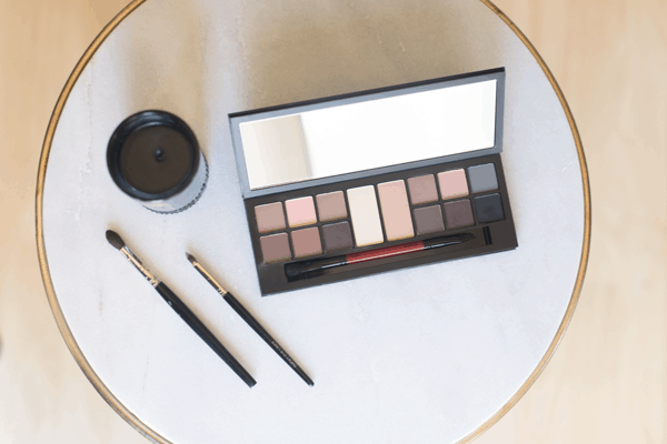 An eyeliner palette on a table next to a few makeup brushes and a candle. 