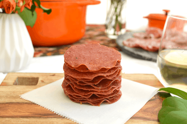 A stack of salami chips on a piece of parchment paper on top of a cutting board.