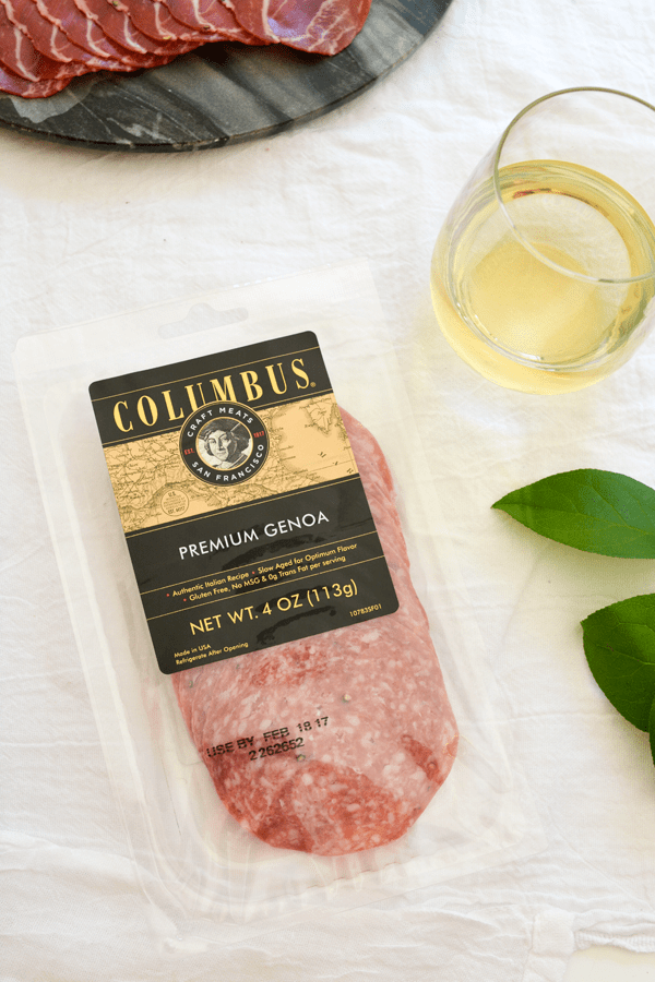 Package of genoa salami on top of a table, next to a glass of wine.