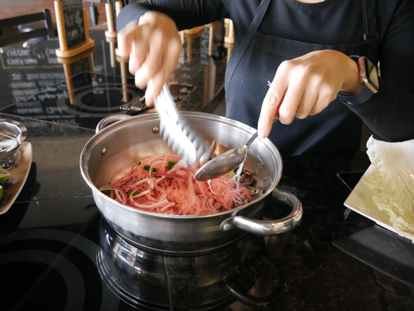 Woman cooking mung bean noodles for a spicy noodle salad in a walk. 