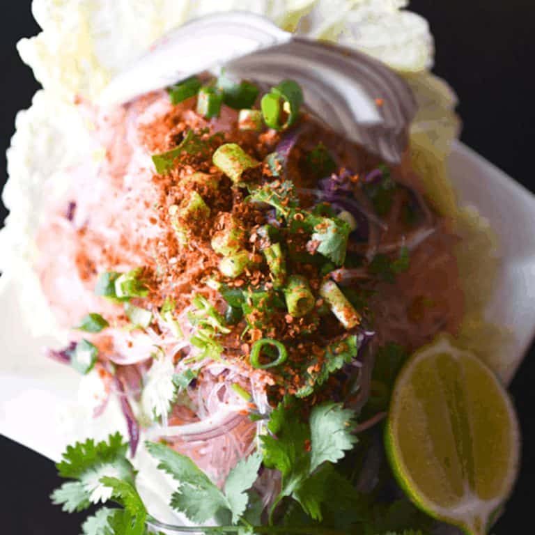 Close up of a spicy Glass Noodle Salad on a white plate topped with chopped green onions and chile flakes.