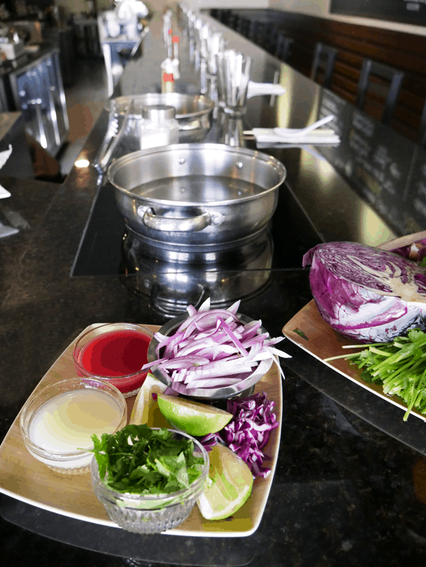 Ingredients to make Spicy Noodle Salad on a plate on a counter next to a hot pot. 