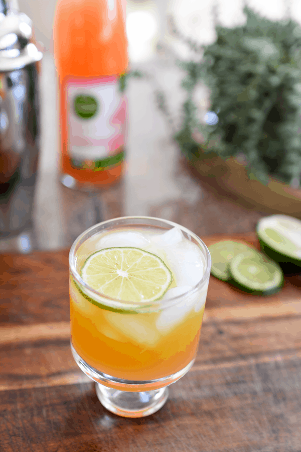 Glass of an easy peach paloma cocktail with a lime slice.