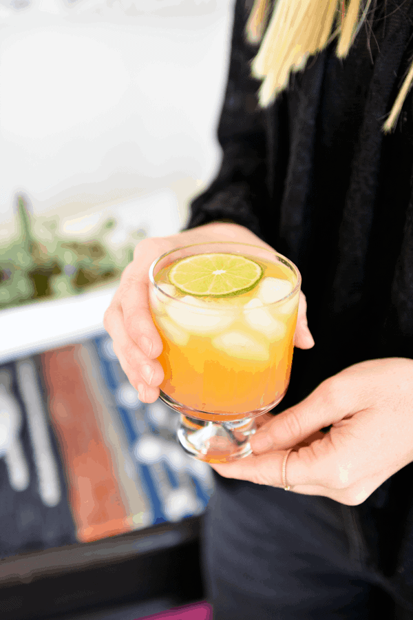 Peach paloma recipe in clear cocktail glass held by a woman in black shirt.