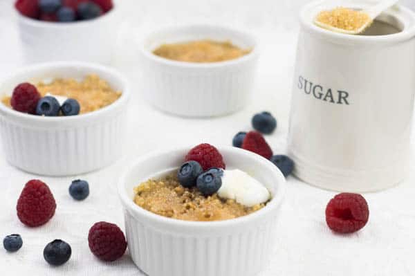 Oatmeal Brûlée in individual white ramekins on a white surface scattered with fresh berries.