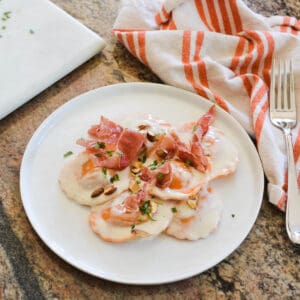 Close up of store-bought butternut squash ravioli on a plate topped with prosciutto and almonds.