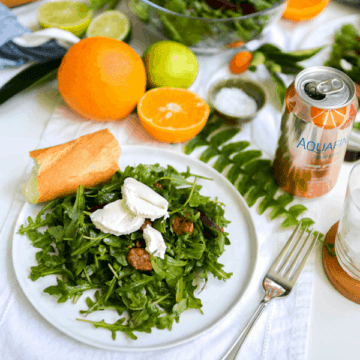 Salad on a plate topped with goat cheese and pecans next to citrus fruit and a canned beverage.