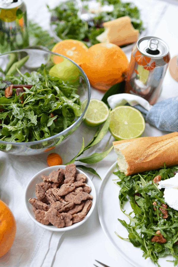 Close up of a small bowl holding candied pecans next to a plate and bowl of salad.