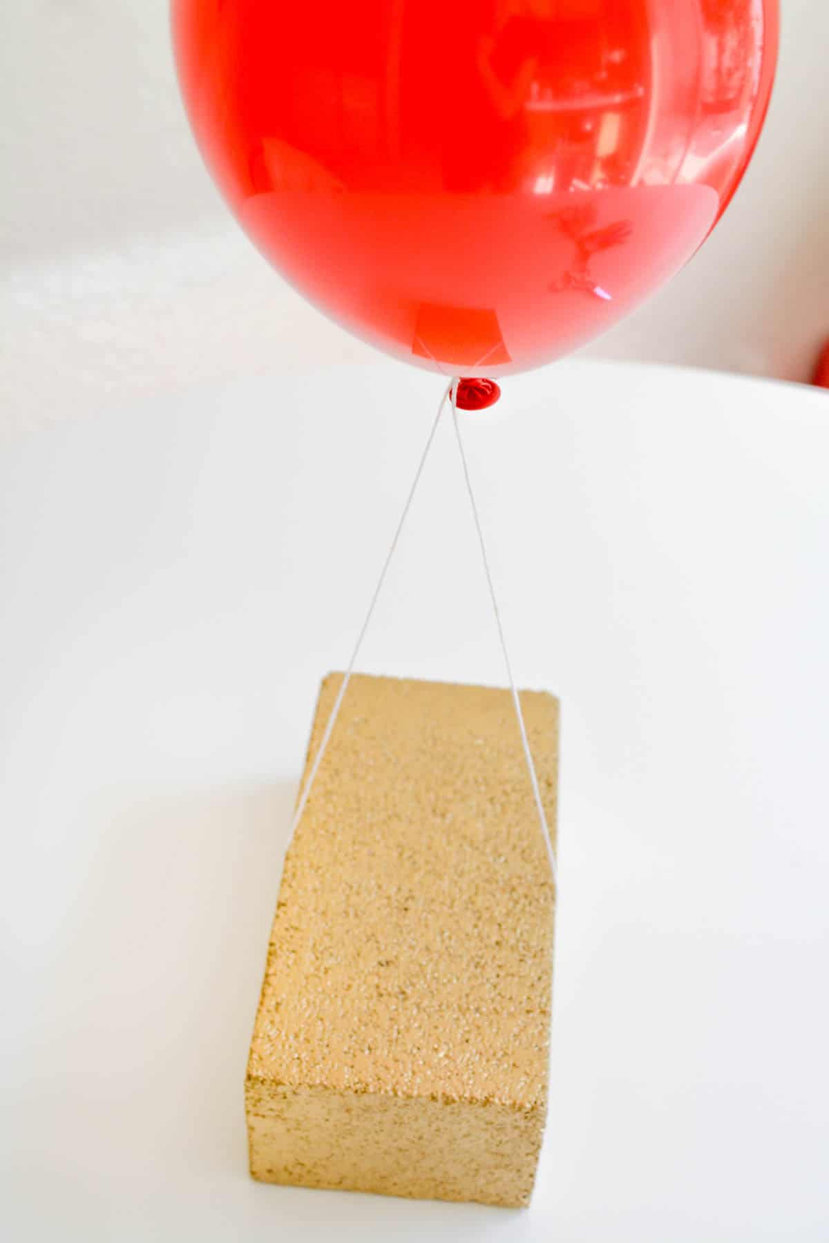 A gold brick holding a red balloon on white string.