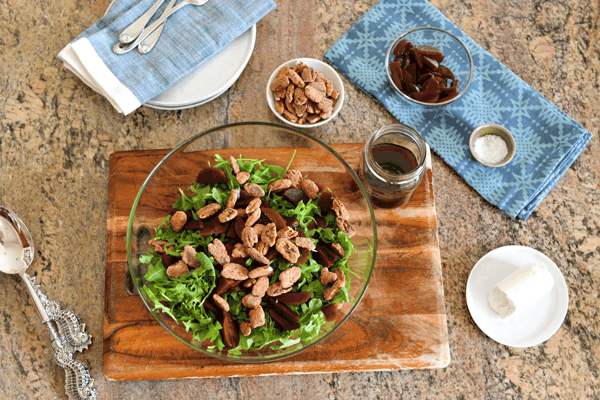 Overhead shot of an arugula salad topped with beets and pecans and a jar of dressing next to it.