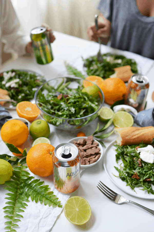 A bowl of salad on a table decorated with fresh citrus and serving plates of salad.