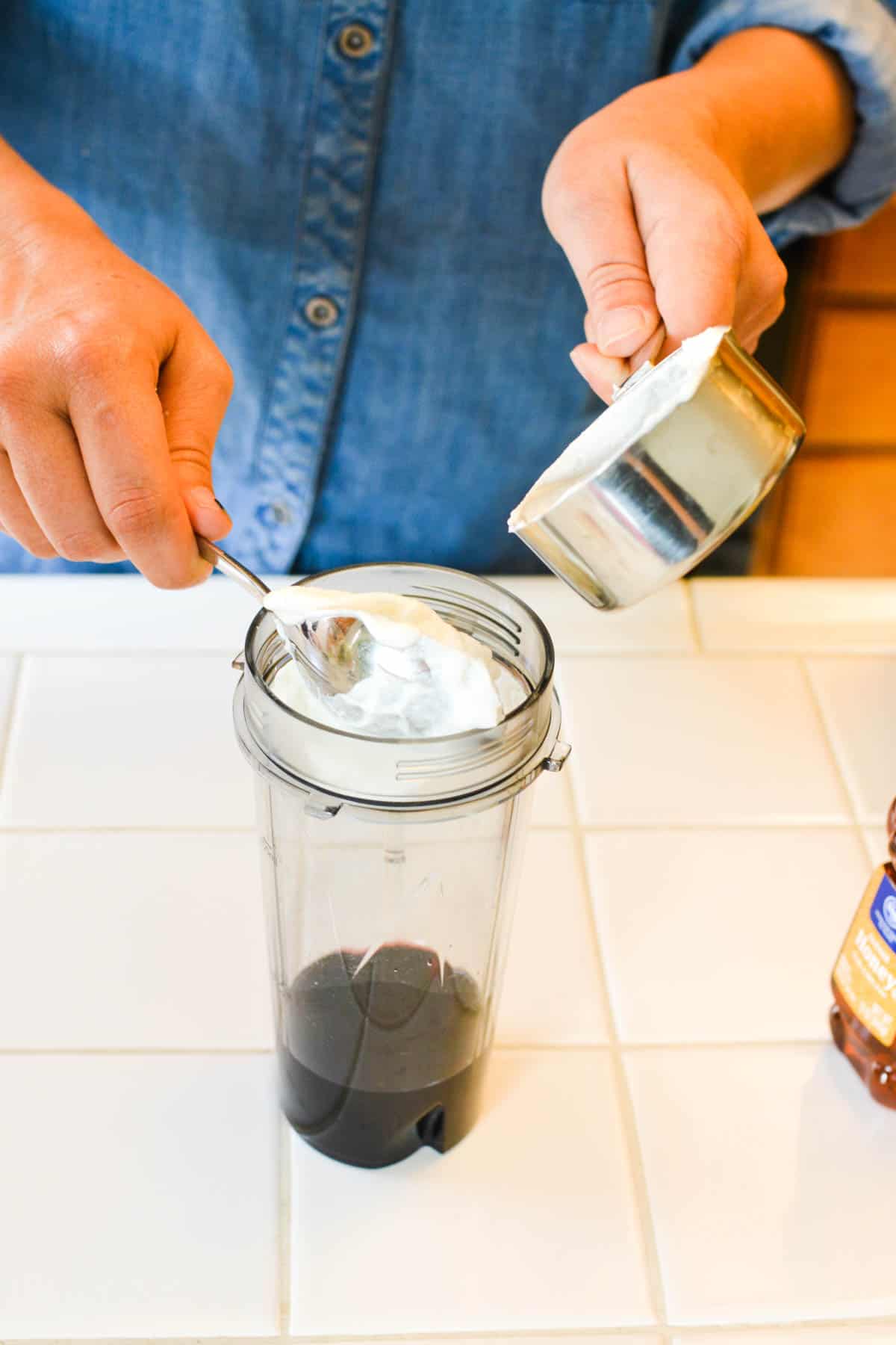 Woman adding yogurt from a measuring cup into a blender jar.