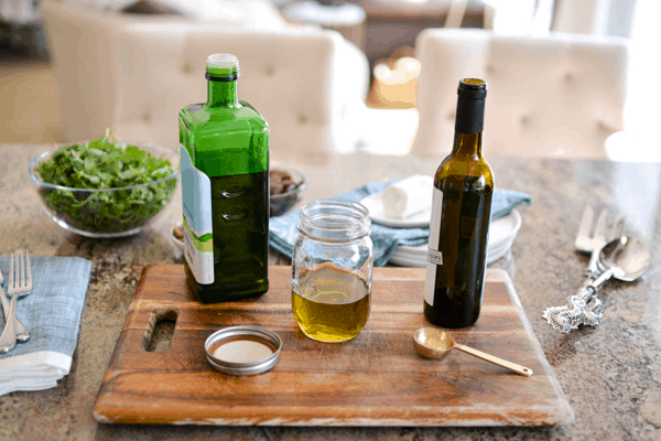 A bottle of olive oil and balsamic vinegar next to a small mason jar holding oil for salad dressing.