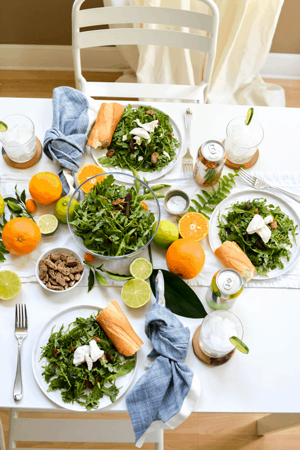 Lunch table with plates of salad and a serving bowl of salad and fresh citrus fruit as the centerpiece.