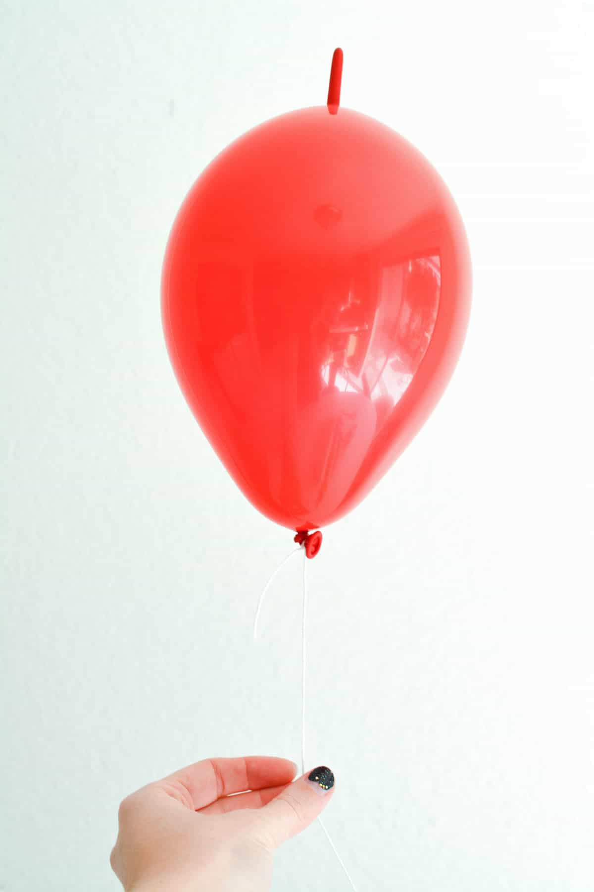 A hand holding a string attached to a small red linking balloon.