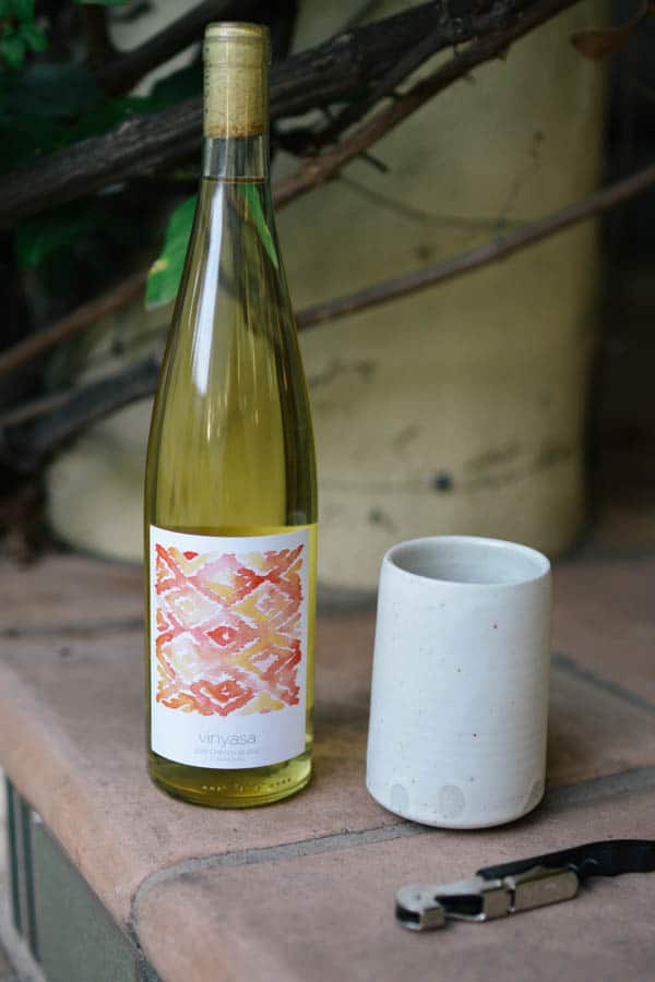 A bottle of wine on a porch with a ceramic glass next to it.