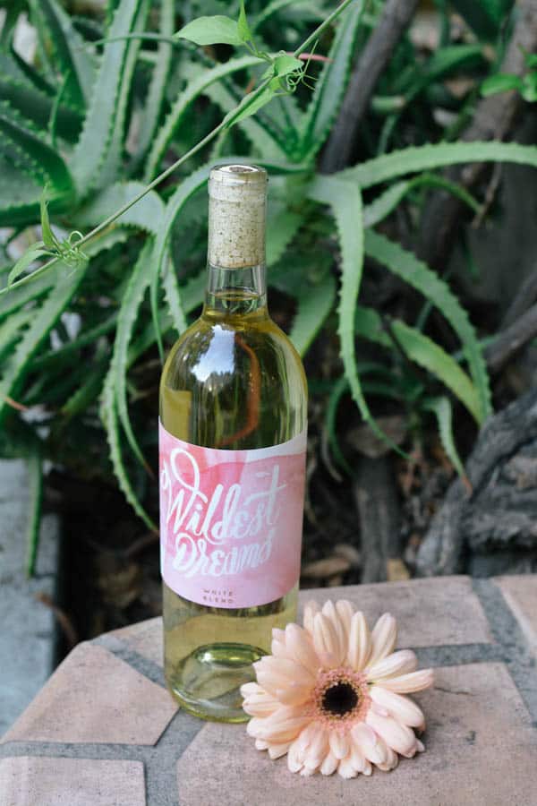 A bottle of wine on a porch with a flower next to it.