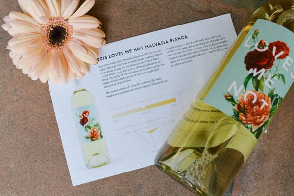 Card with tasting notes next to a flower and a bottle of wine laying on it's side.