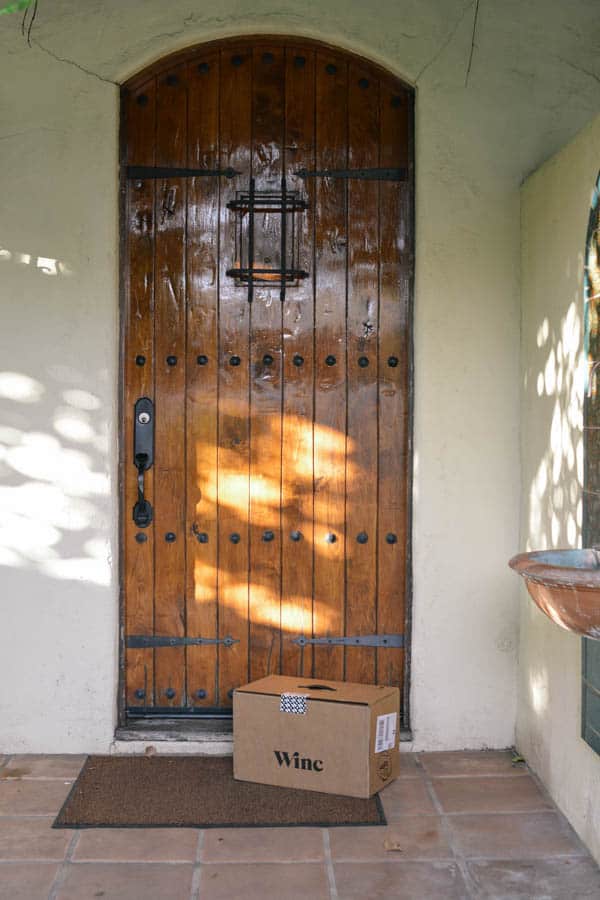 A wooden door with a box of wine on the door mat.