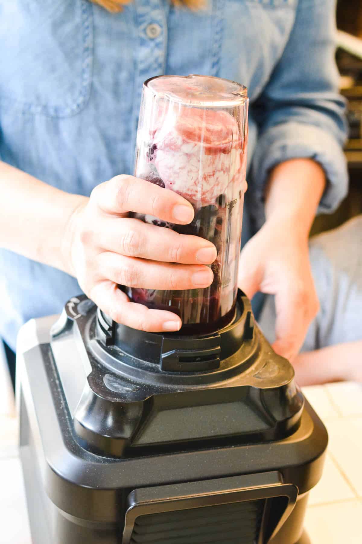 Woman blending a smoothie in an individual sized smoothie cup on a blender. 