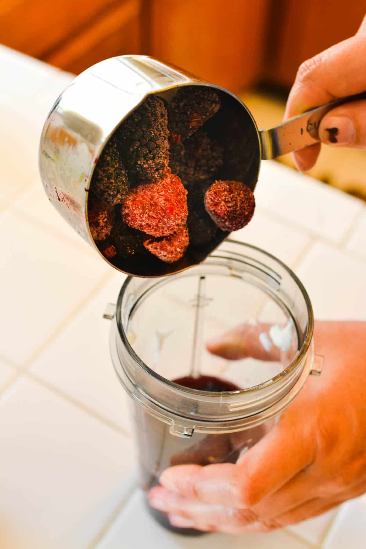 Woman adding frozen red berries to a blender jar for a smoothie.