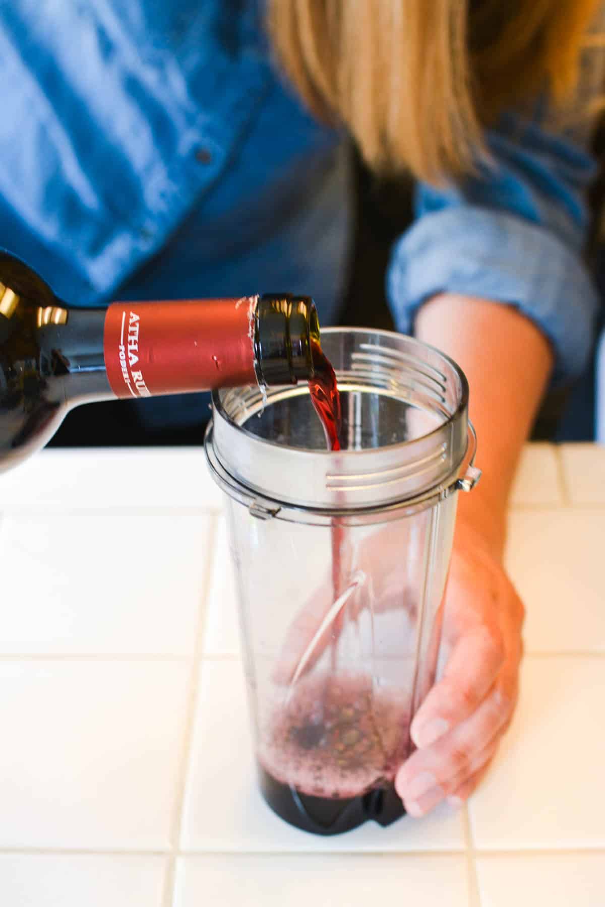 Woman pouring red wine from a bottle into a blender jar to make a smoothie.