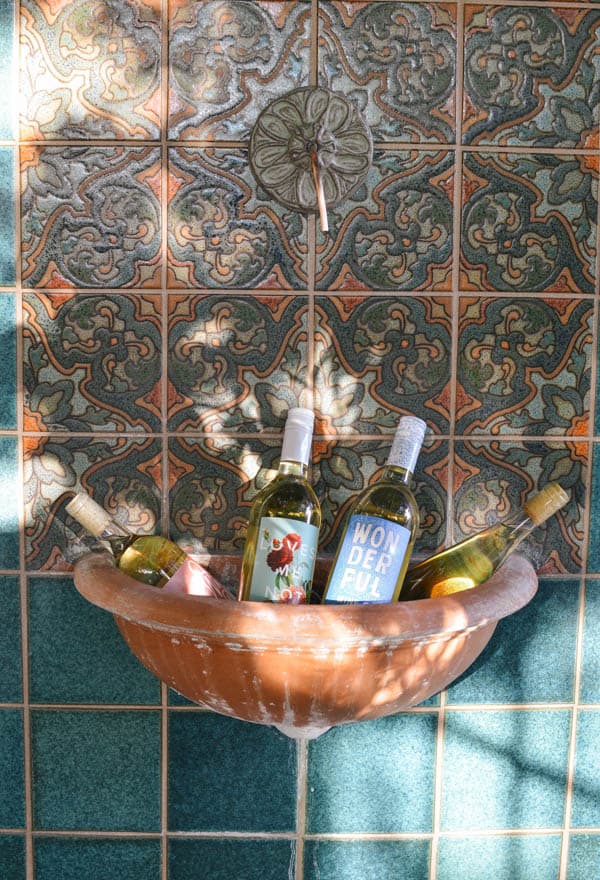 A bunch of wine bottles in the pool of a fountain on a wall. 
