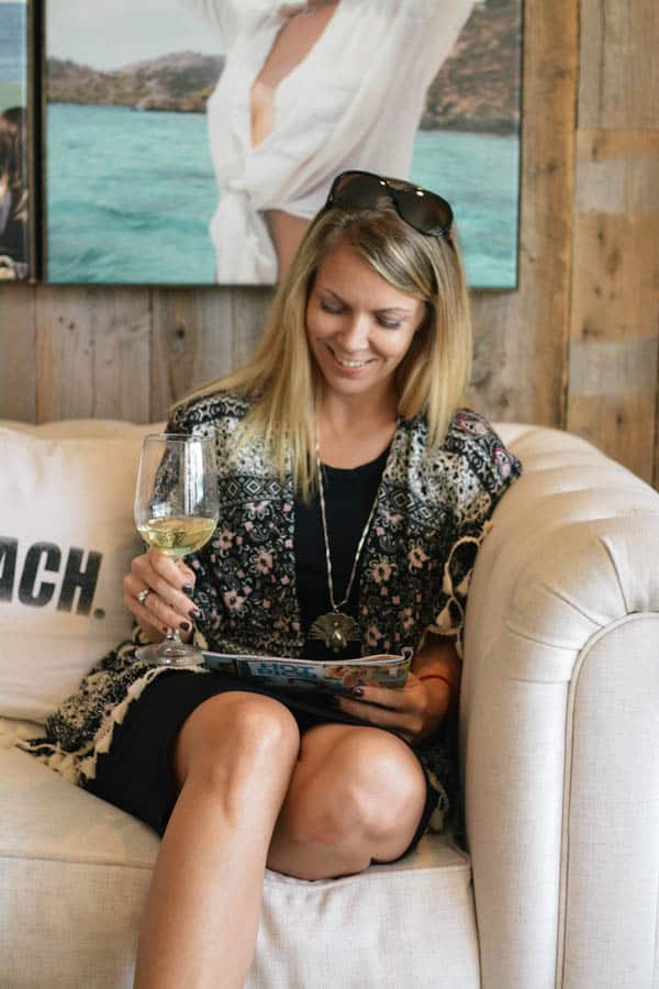 Woman sitting on the couch holding a glass of wine reading a magazine. 