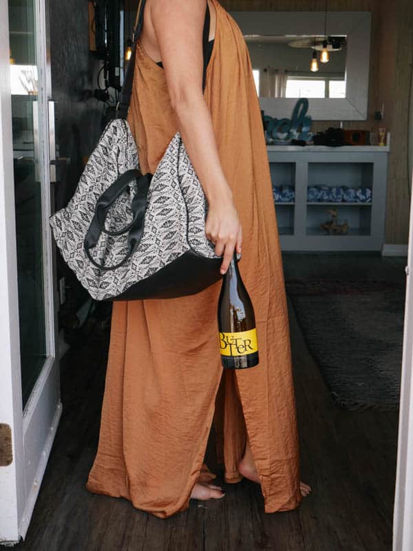 Woman holding a weekender bag and a bottle of chardonnay. 