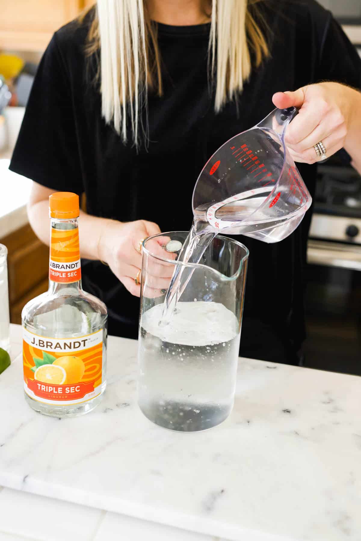 A woman pouring a measuring cup of Triple Sec into a pitcher for margaritas.