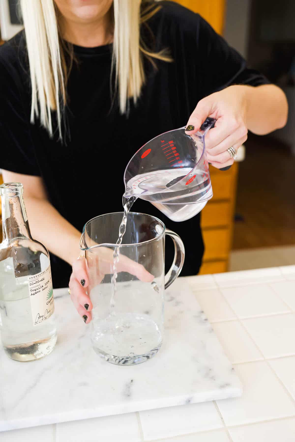 woman adding tequila to a pitcher to make margaritas for a party.