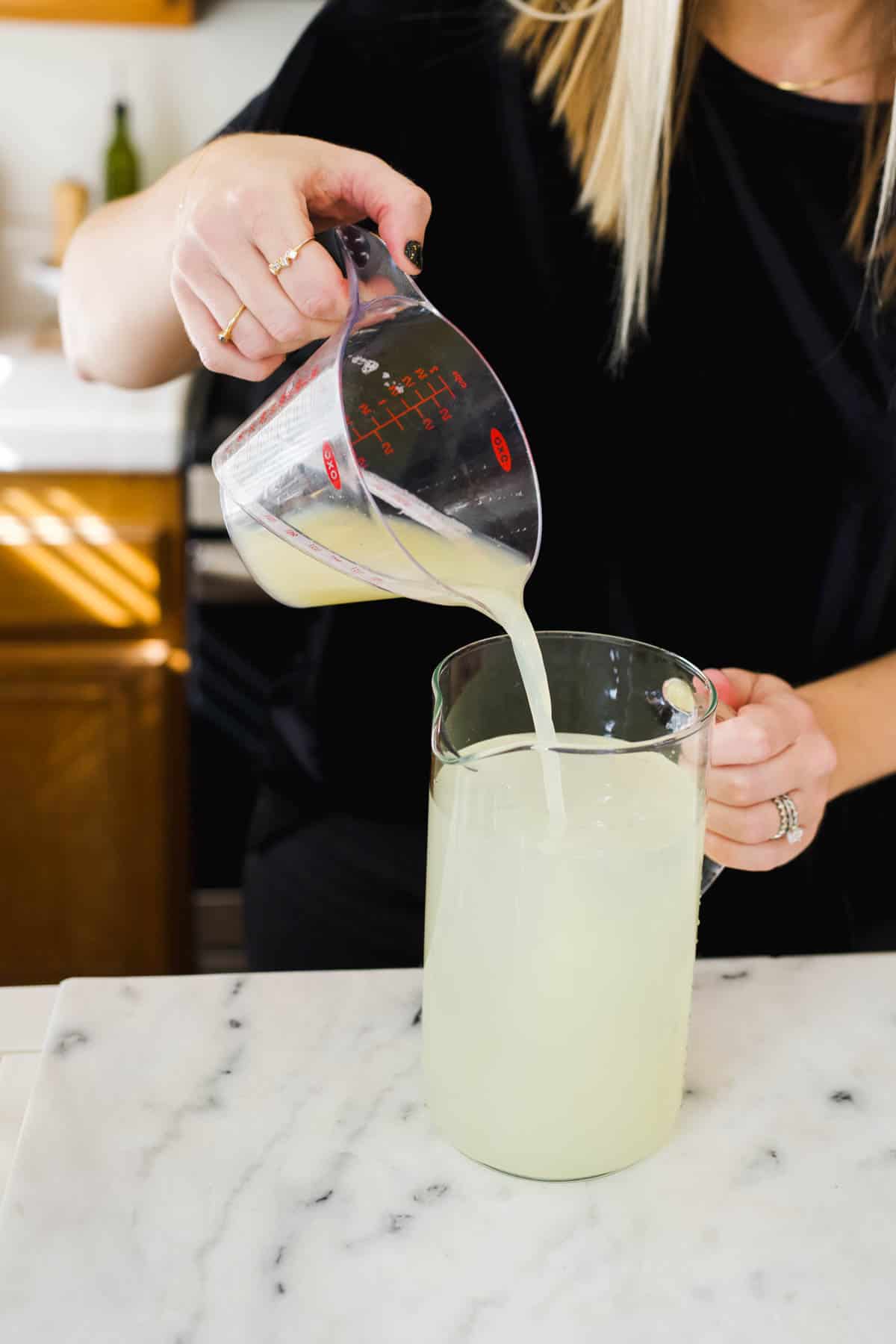 Woman adding fresh lime juice from a measuring cup into a pitcher.