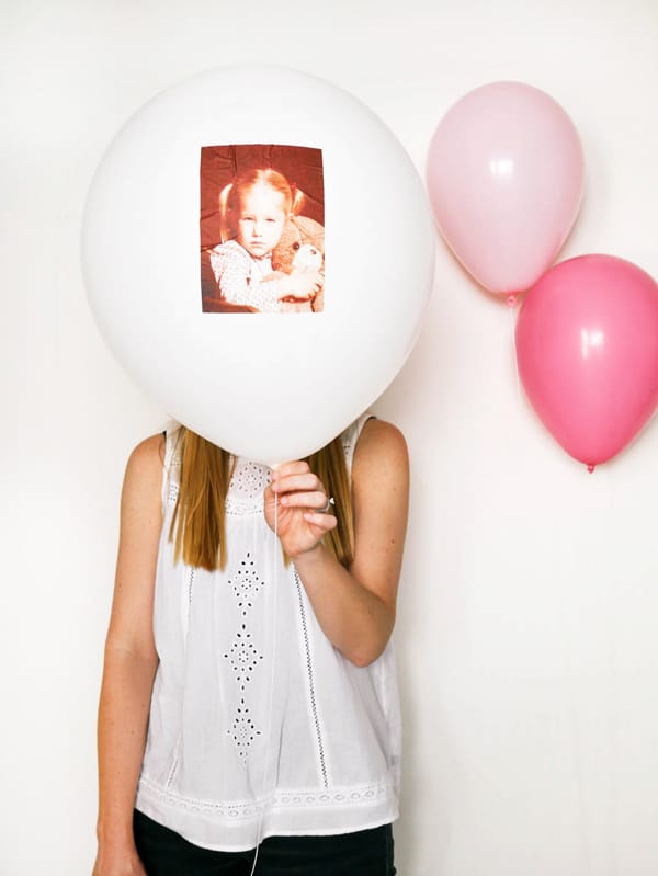 Woman holding a large white balloon with a baby photo on it in front of her face. 