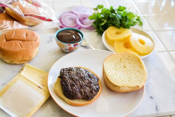 A Bubba Burger patty on a hamburger bun with other toppings including pineapple on the counter near it. 