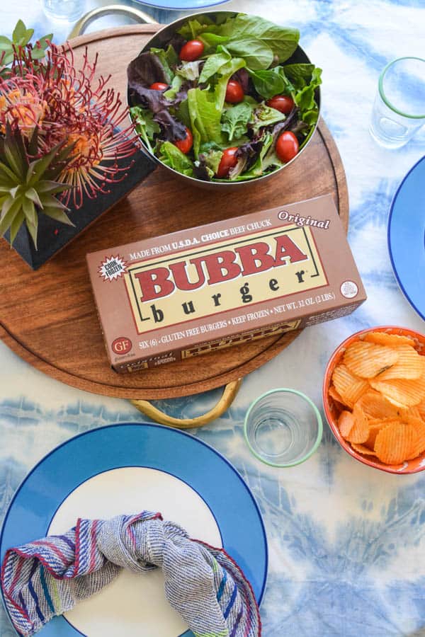 A box of Bubba Burger patties on a tray on a table next to a bowl of salad. 