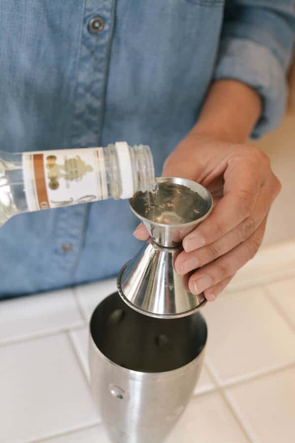 Woman measuring coconut rum in a cocktail jigger. 