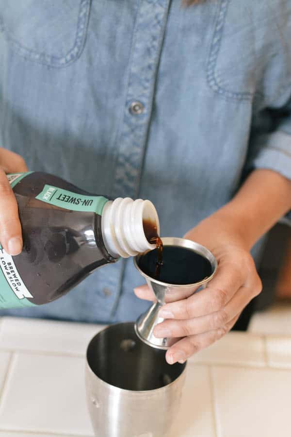 Woman measuring cold brew coffee in a cocktail jigger. 