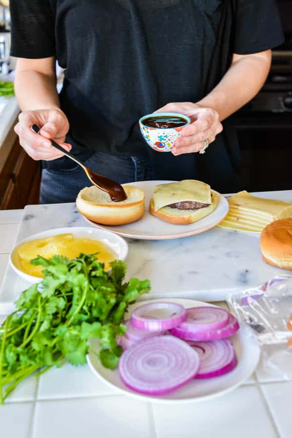 Woman spooning barbecue sauce on  a hamburger bun. 