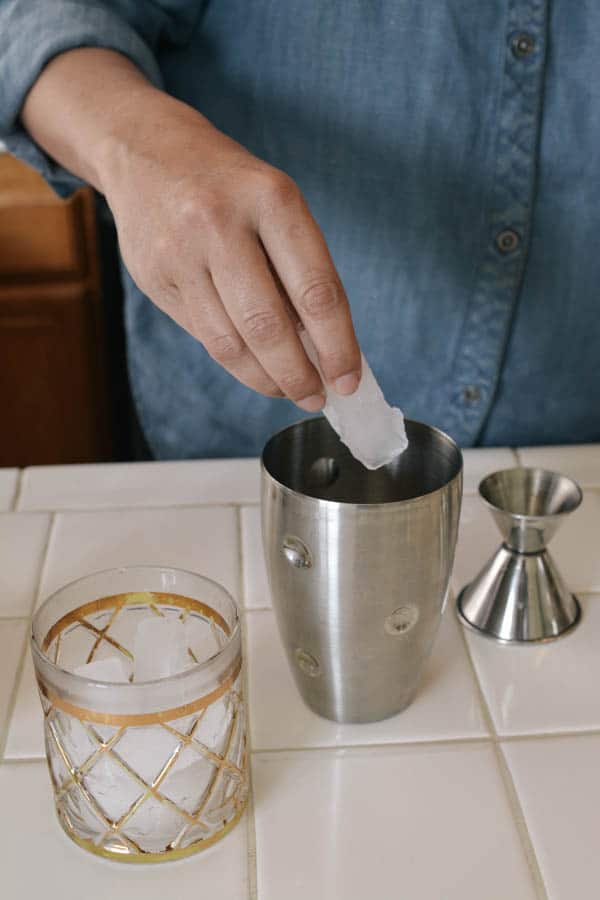 Woman adding ice to a cocktail shaker. 