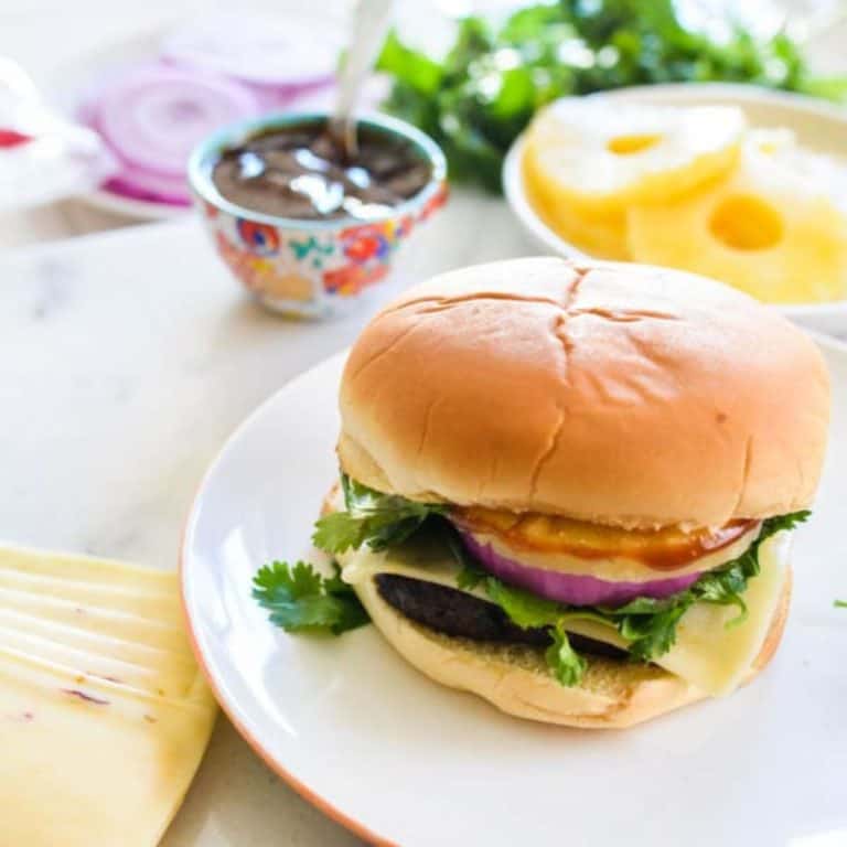 Close up of a burger with pineapple and barbecue sauce on a plate.