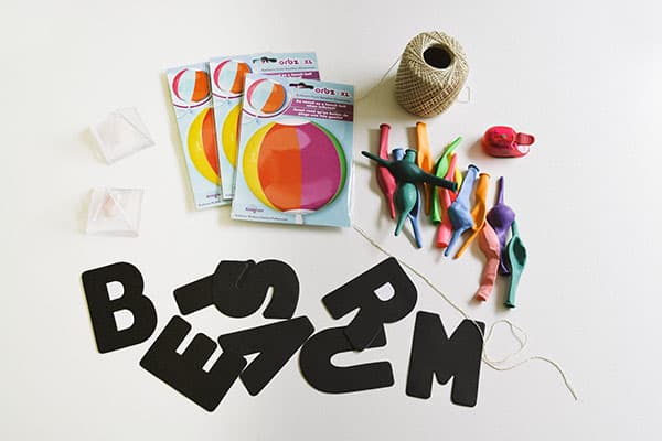 Supplies you will need to make a balloon decoration for a summer party on a white surface.